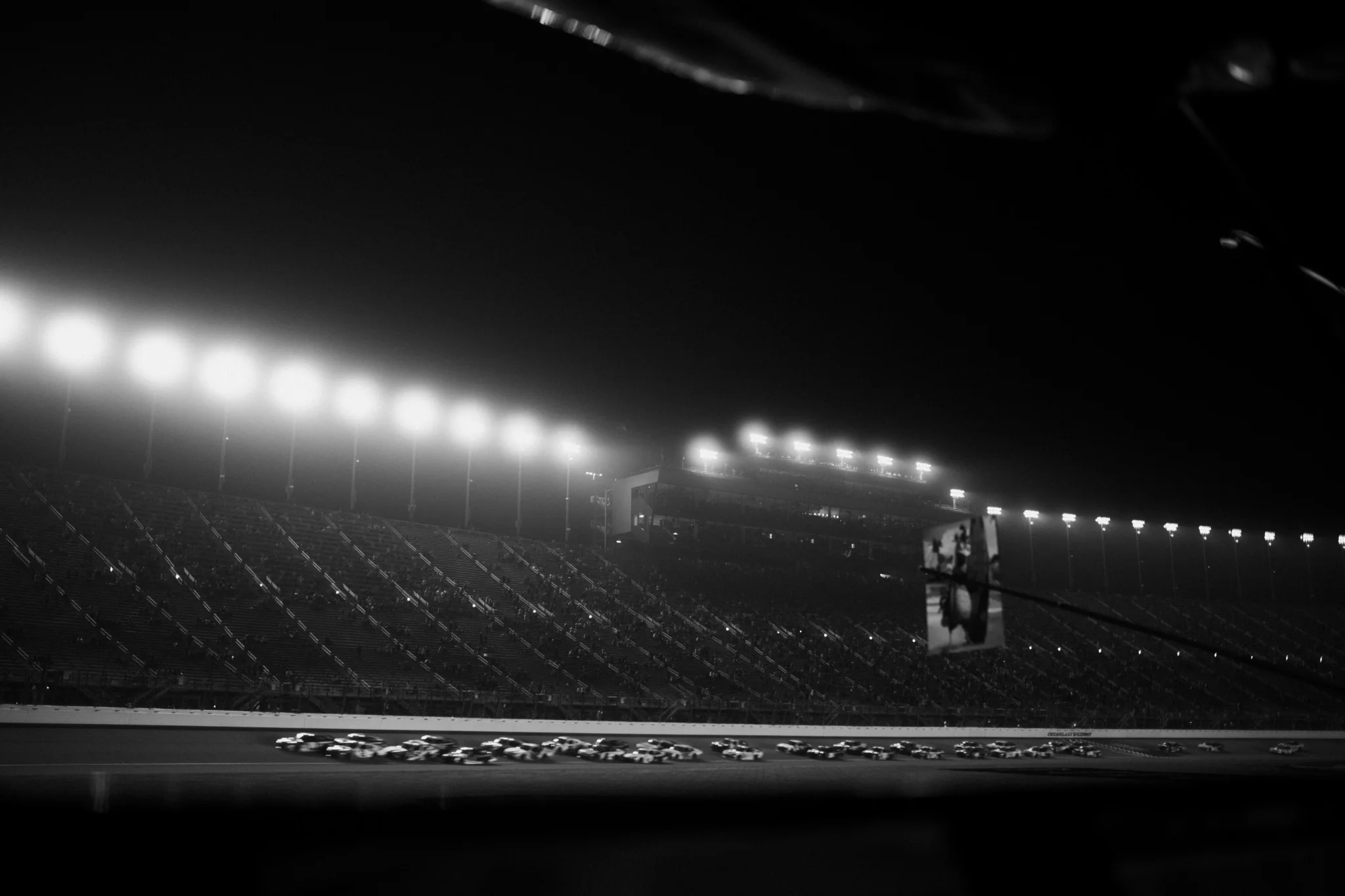 NASCAR field racing beneath speedway lights at night