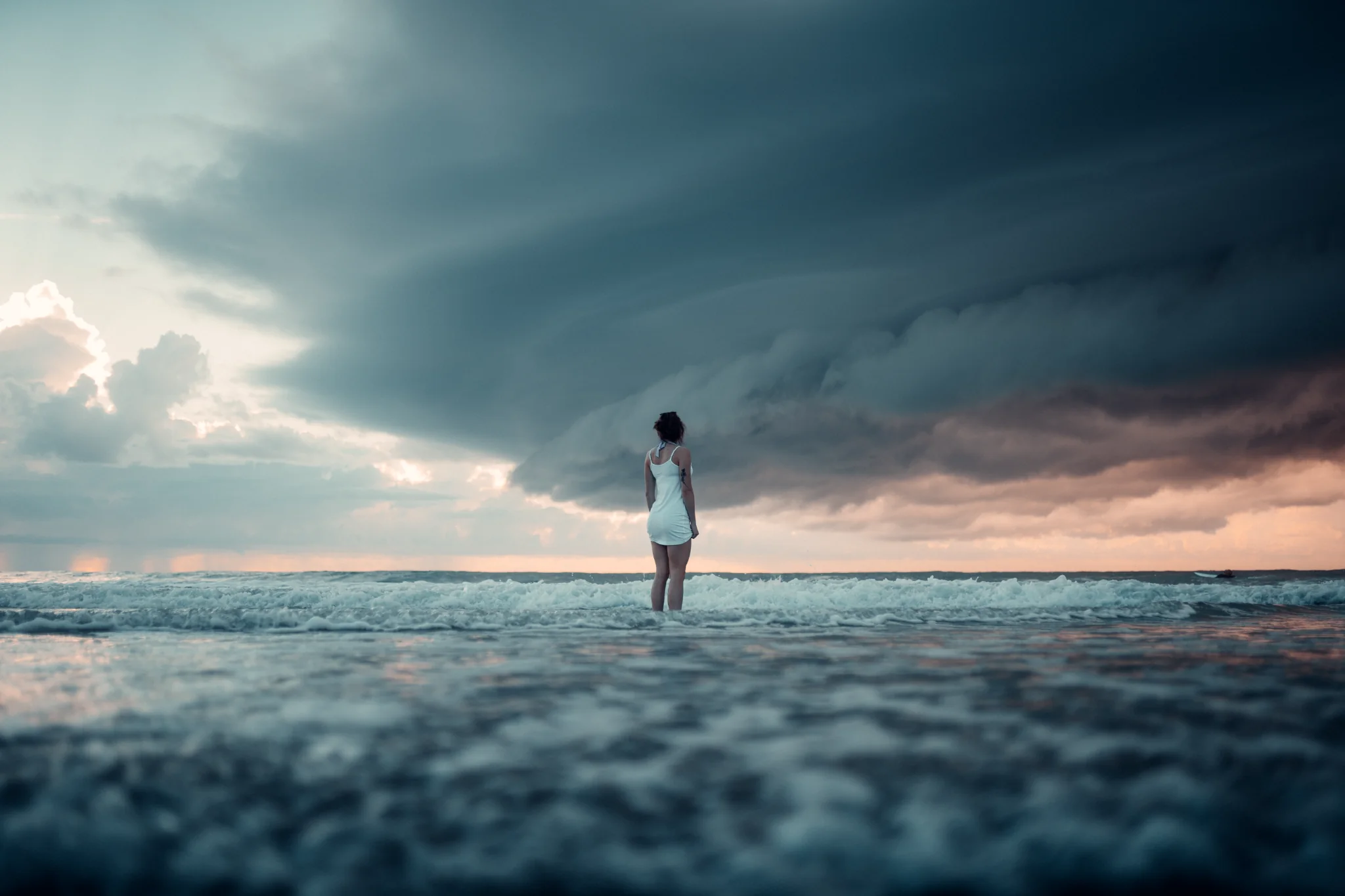 Person standing in the ocean beneath a dramatic storm shelf cloud